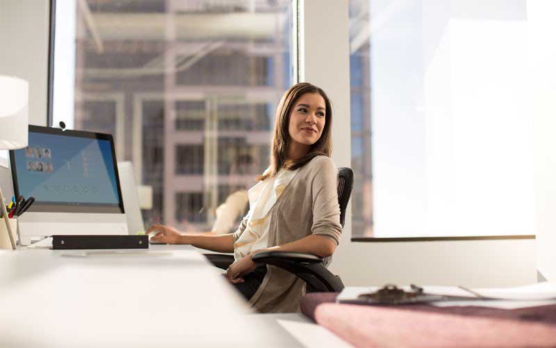 Jonge vrouw aan bureau met laptop die in haar stoel ligt.
