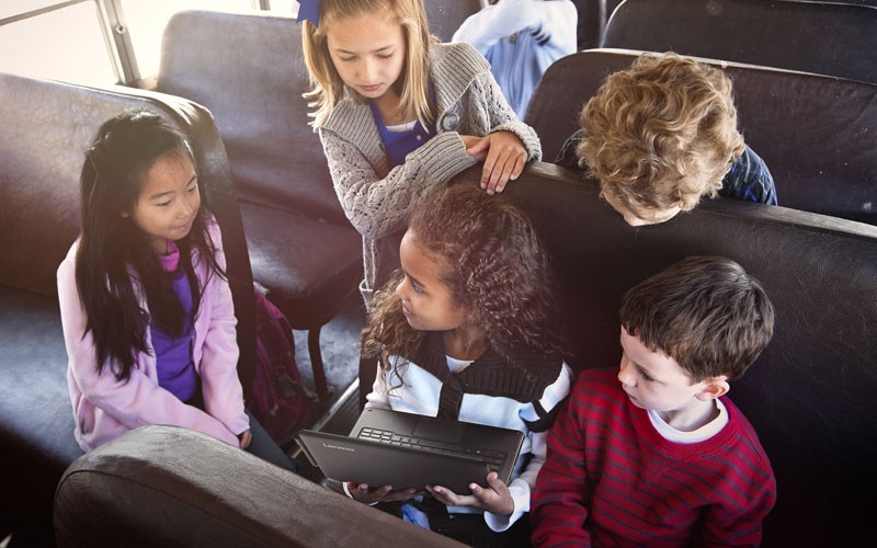 Jonge leerlingen zitten in een bus met een Lenovo laptop