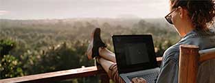 Een vrouw met bril werkt op het balkon op haar laptop