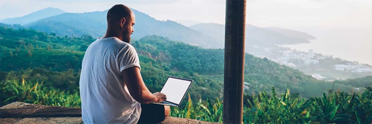 Een man werkt op zijn laptop in een groene heuvelachtige omgeving