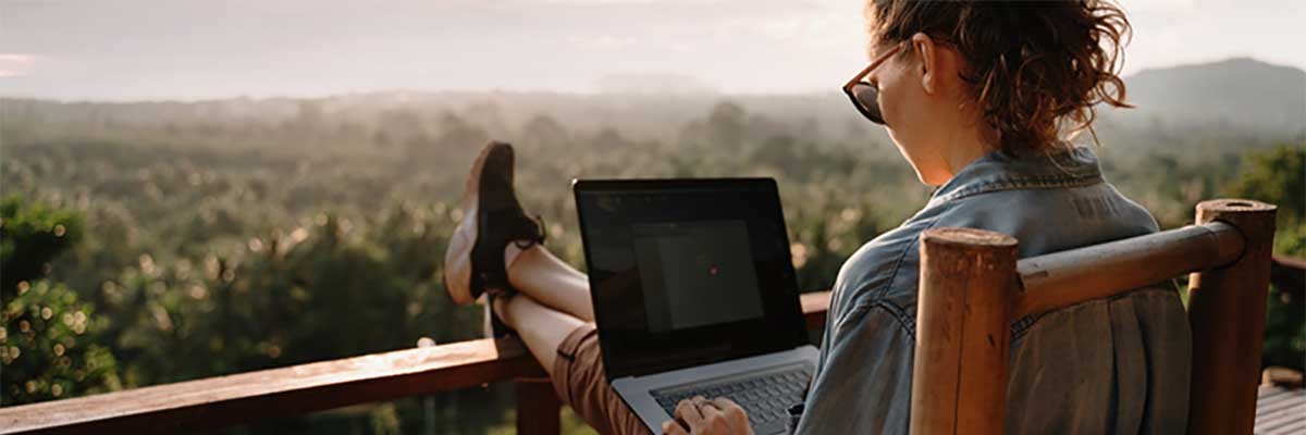 Een vrouw werkt op haar laptop met uitzicht over natuur