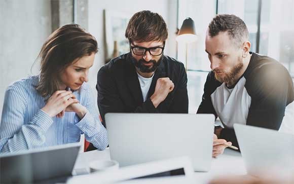 Drie collega's lezen een IT-rapport op hun laptops