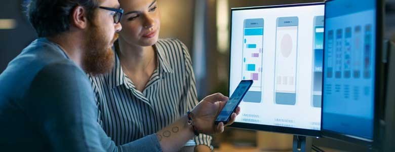 Designers bekijken het ontwerp van een smartphone op twee monitoren 