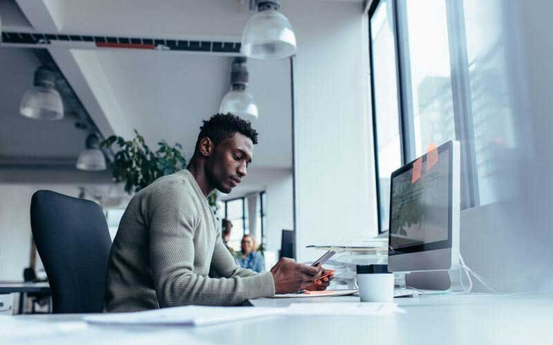 Man achter zijn bureau kijkt op zijn smartphone